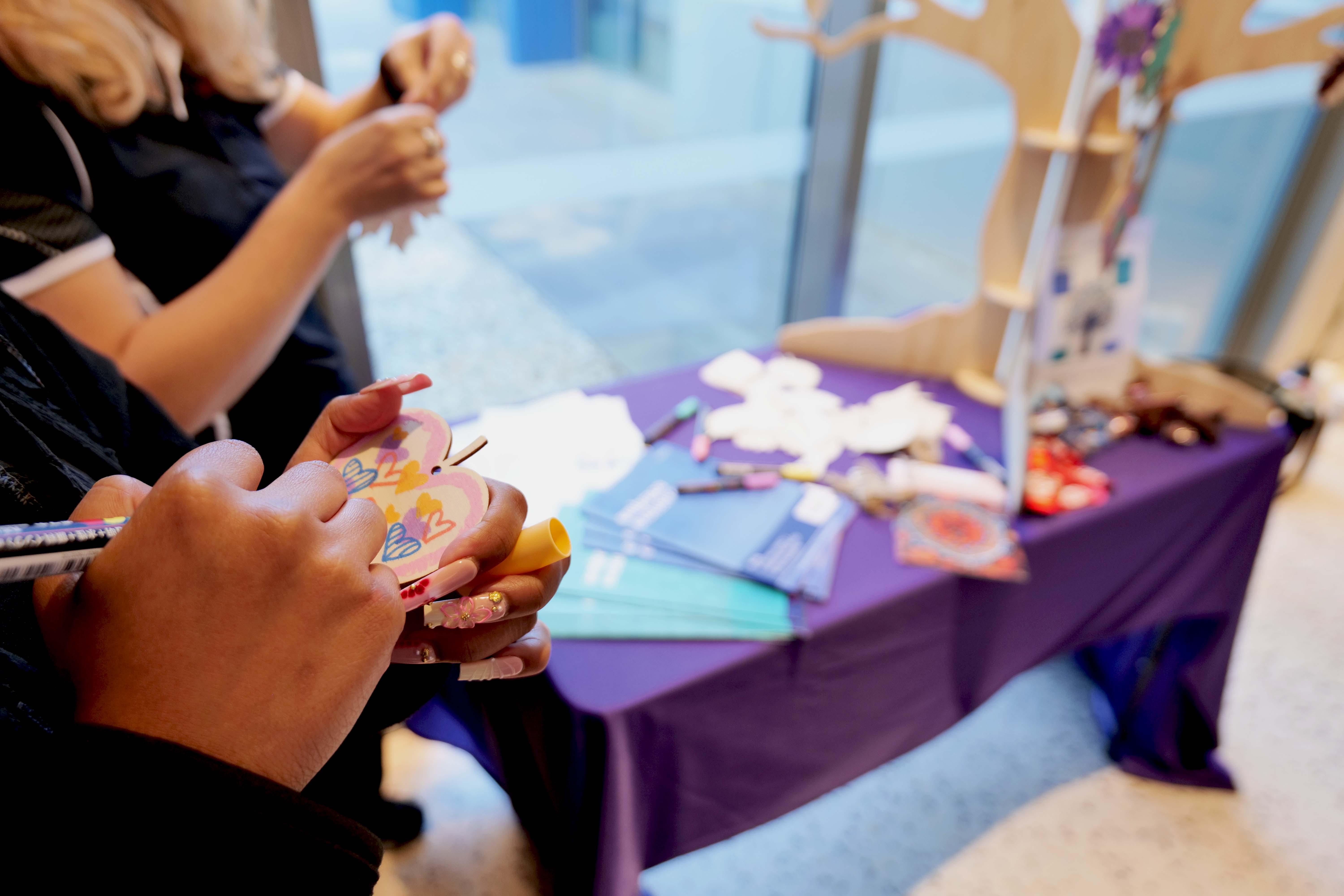 A hand decorating a wooden leaf using a paint pen